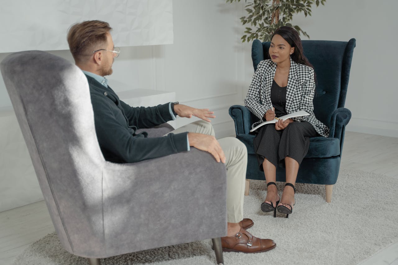 Two professionals conducting an interview in a modern office with stylish chairs and a white backdrop.